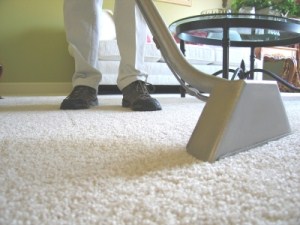 Person vacuuming a carpeted floor with a vacuum cleaner in a living room